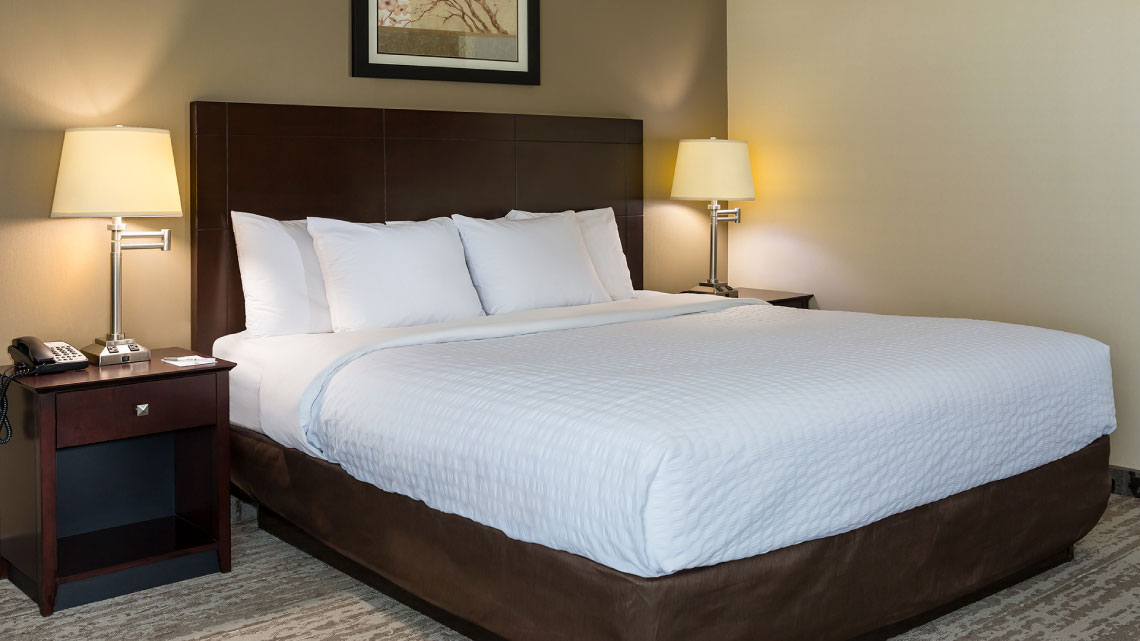 large size bed with nightstands, lamps, white linens, dark brown wood in hotel room