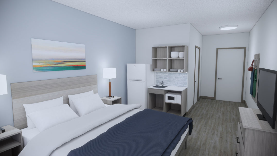 bed in a hotel room with white and blue linens against a light gray wall with a refrigerator, small kitchen, TV, hardwood floors