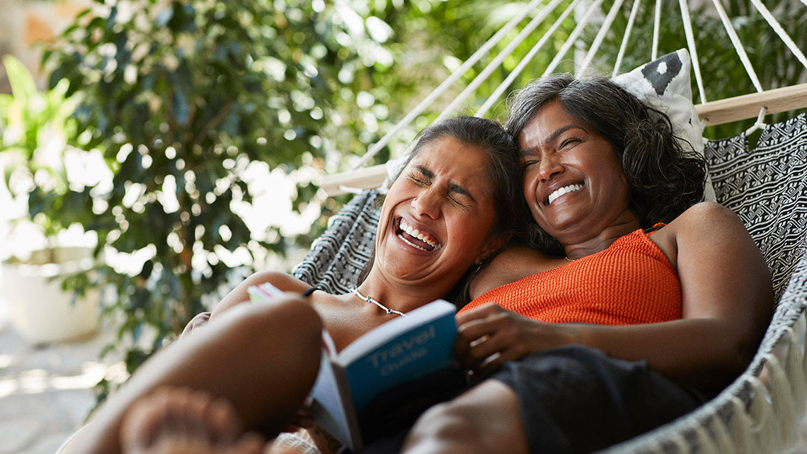 woman and daughter in hammock outside laughing and reading book