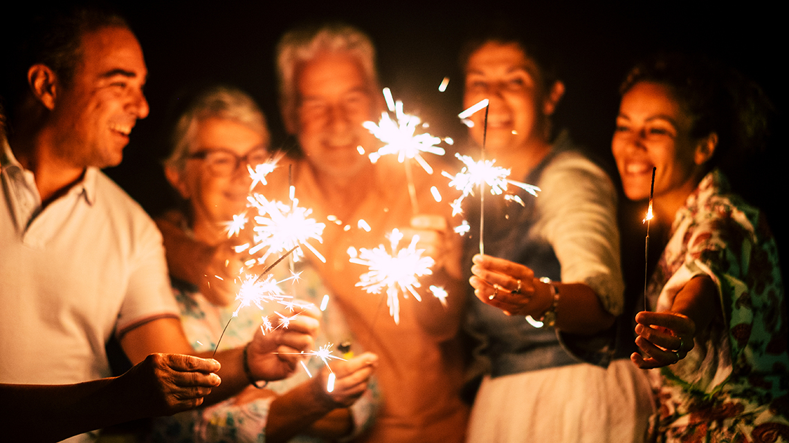 Group of people have fun celebrating together new year eve or birthday with sparkles light and fireworks in friendship outdoor at evening time - family and friends different ages celebrate friendly and smiling