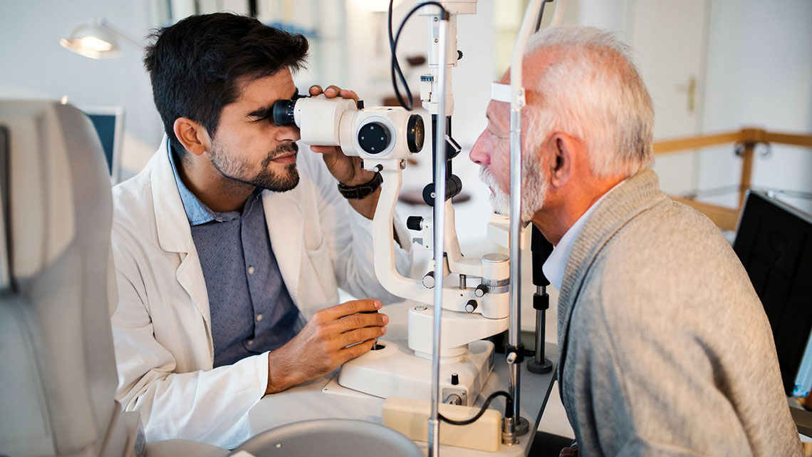 male eye doctor looking through the eye exam machine with an older man patient looking into the machine