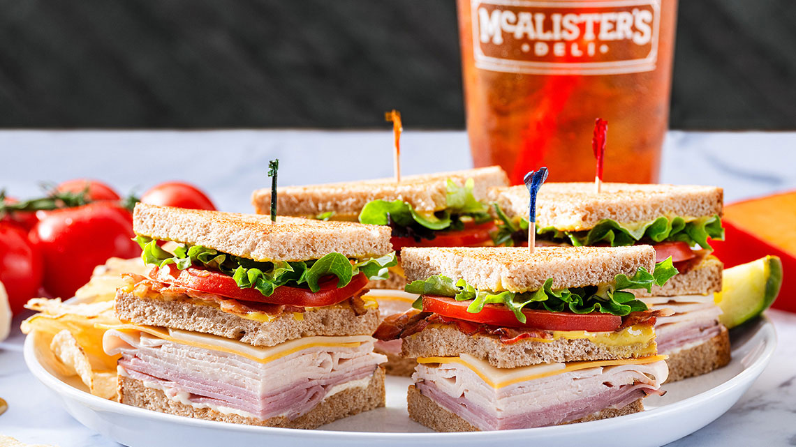 classic club sandwich on a plate with ice tea drink