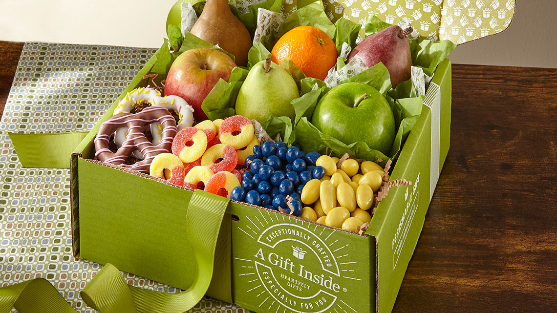 green gift box of chocolate covered pretzels, gummy circles, candy coated berries, nuts, pears, apples, oranges