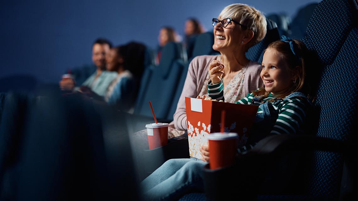 Happy little girl and her grandmother enjoying in movie projection in cinema.