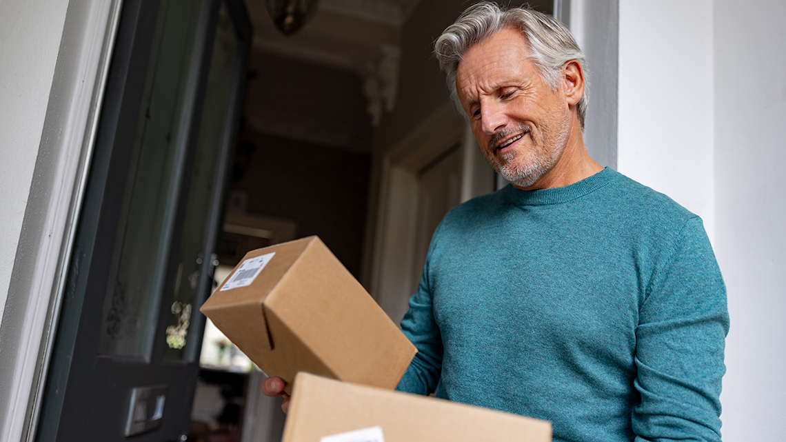 Portrait of a senior man receiving packages in the mail at home and reading the labels at the door - online shopping concepts