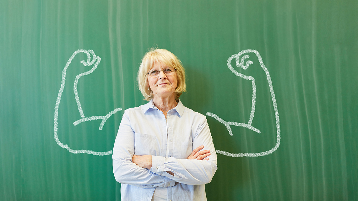 Strong senior teacher with chalk muscles in front of chalkboard
