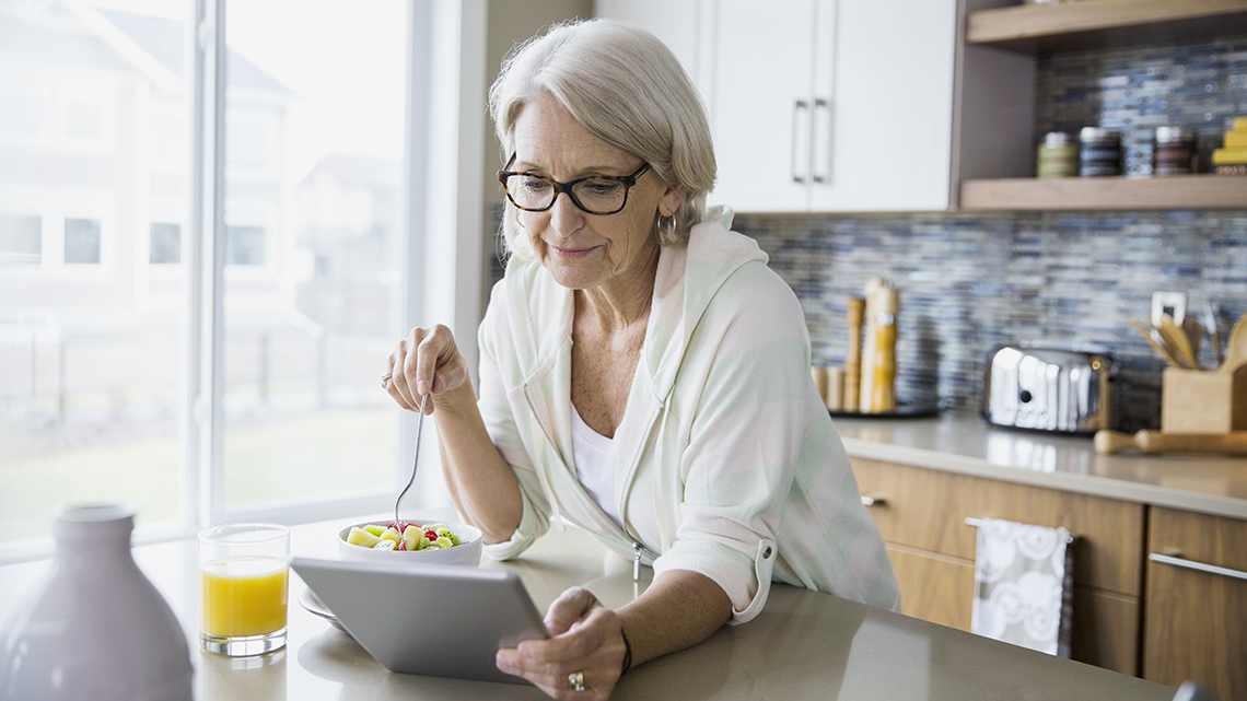 woman in kitchen eating while on tablet