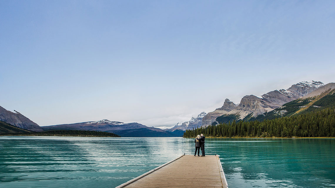 Couple standing end pier, lake, mountains