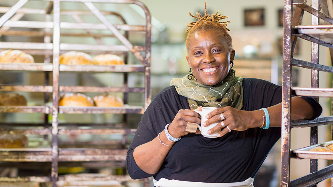 african american woman holding coffee mug with racks of baked bread