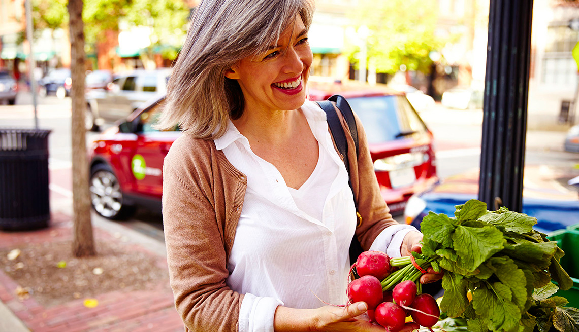 Mujer sonriendo en una calle frente a un puesto de frutas y vegetales