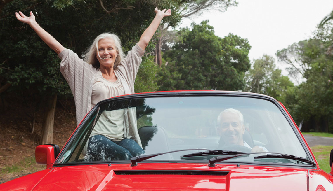 mature couple driving a red car 