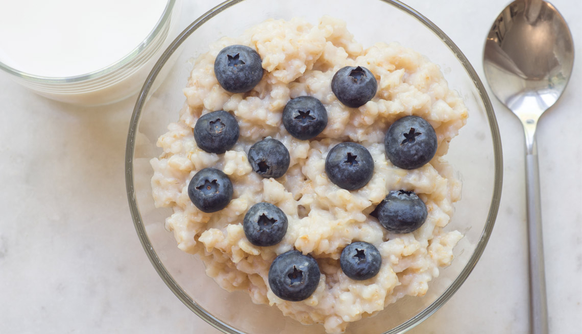Bowl of oatmeal with blueberries, a glass of milk and spoon.