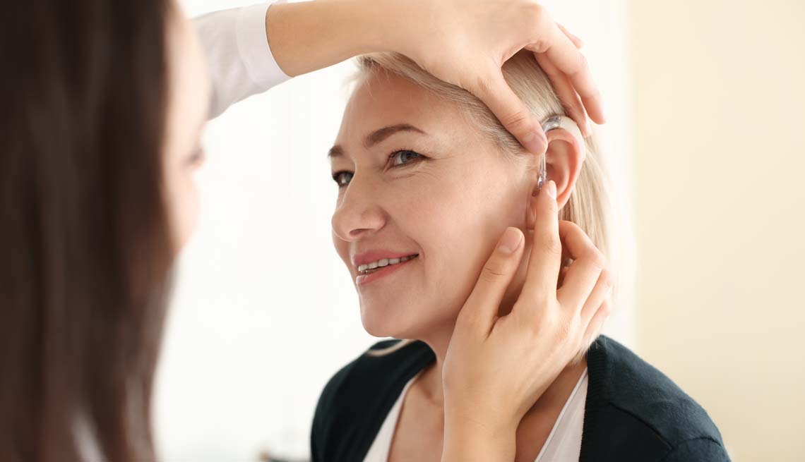 Doctor putting a hearing aid in woman's ear