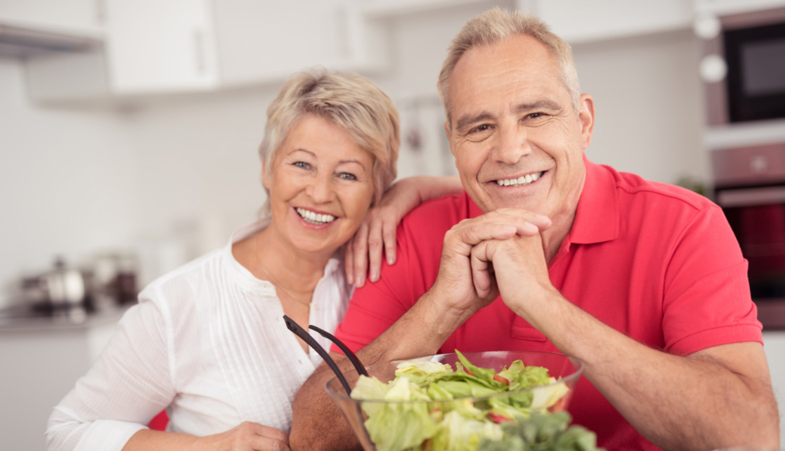 Couple in a home kitchen serving a bowl of salad