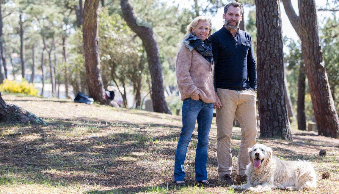 Man and woman walk through a wooded park with their dog
