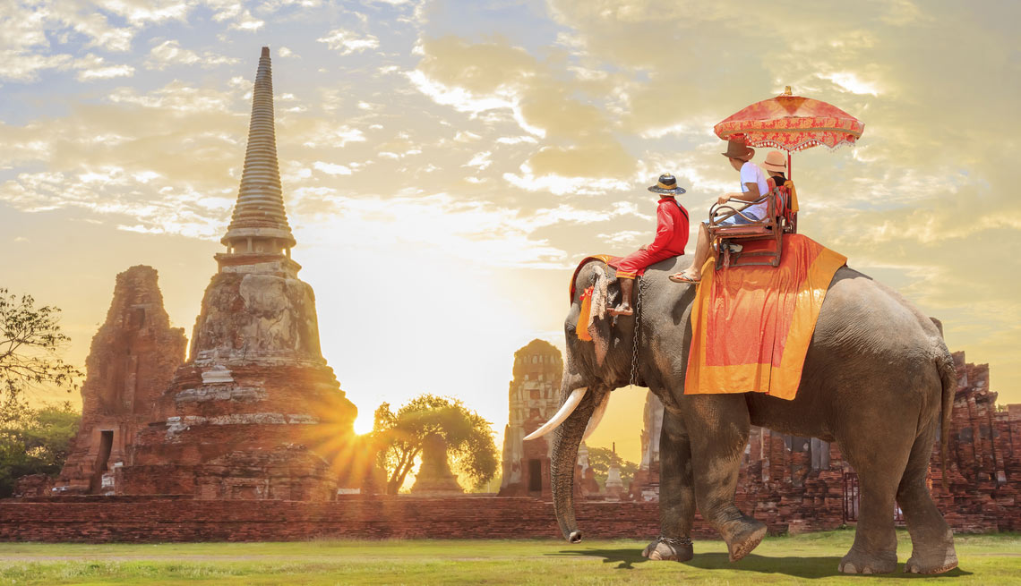 Three people riding and elephant through Thailand landscape