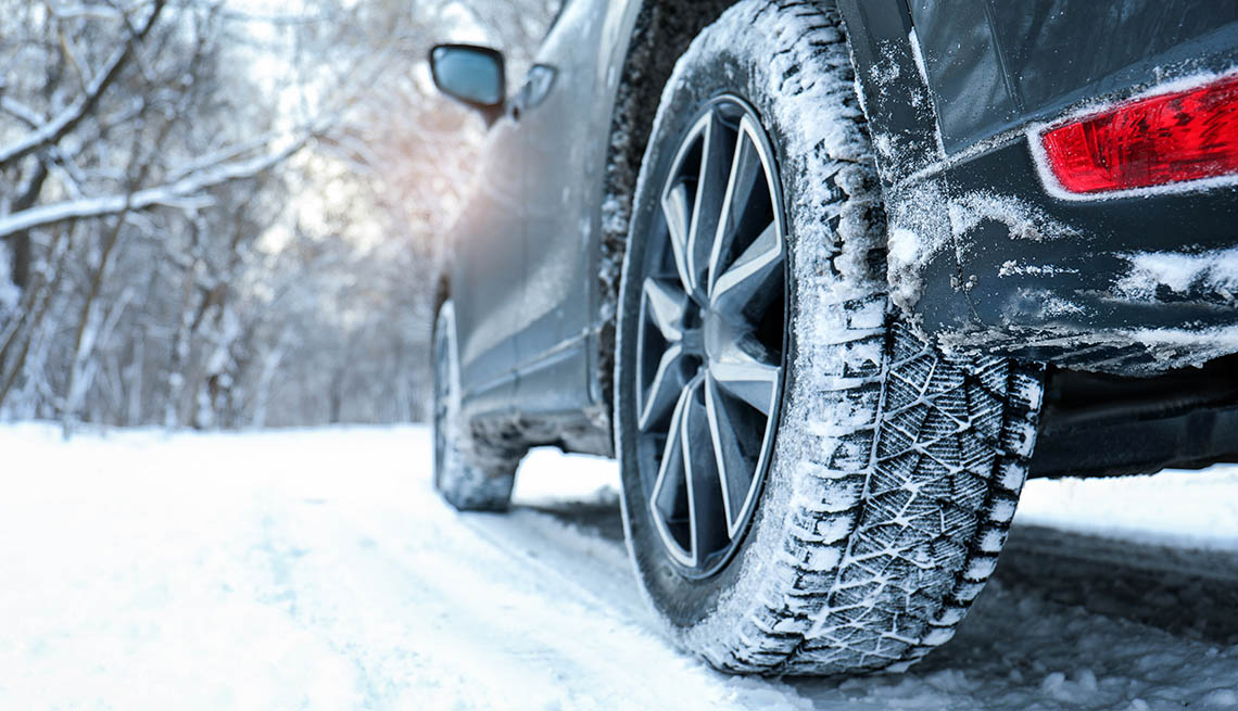 Close up of a vehicle tire driving down a snow covered road