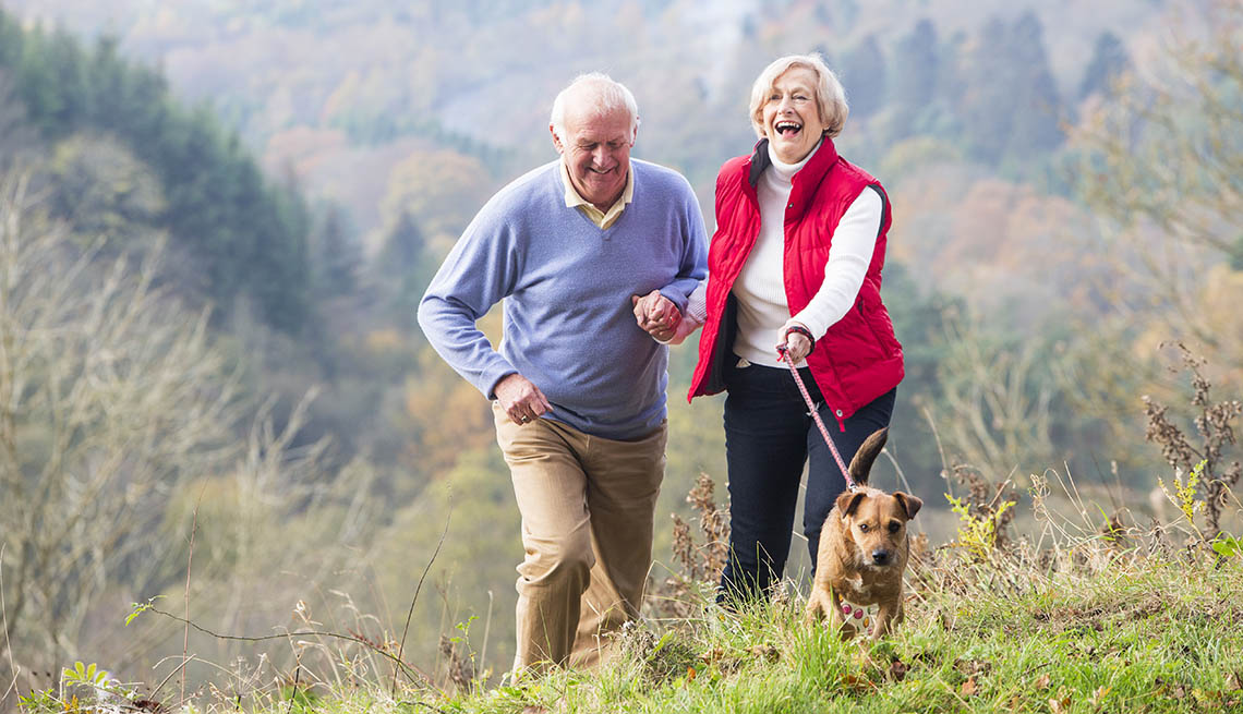 A happy senior couple smile as they walk their dog through the countryside.