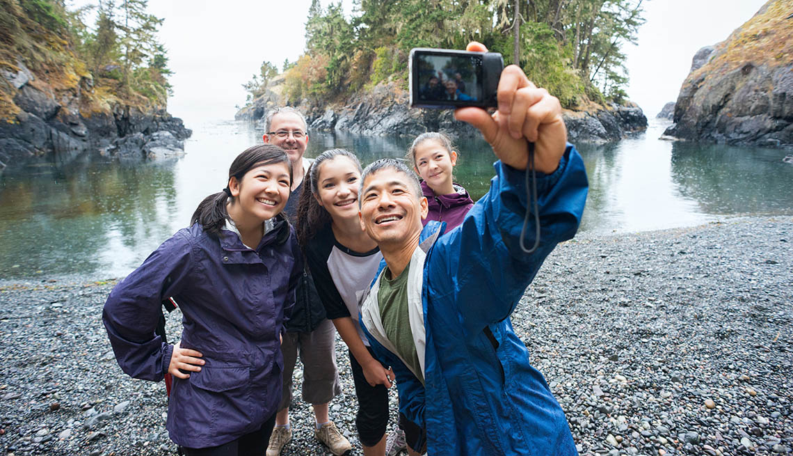 A real extended family of multi-ethnic and multi-generational backpackers in the wilderness pose of a selfie on a deserted beach surrounded by islands and forest with the ocean in the background.  Rainy day in a wilderness park.