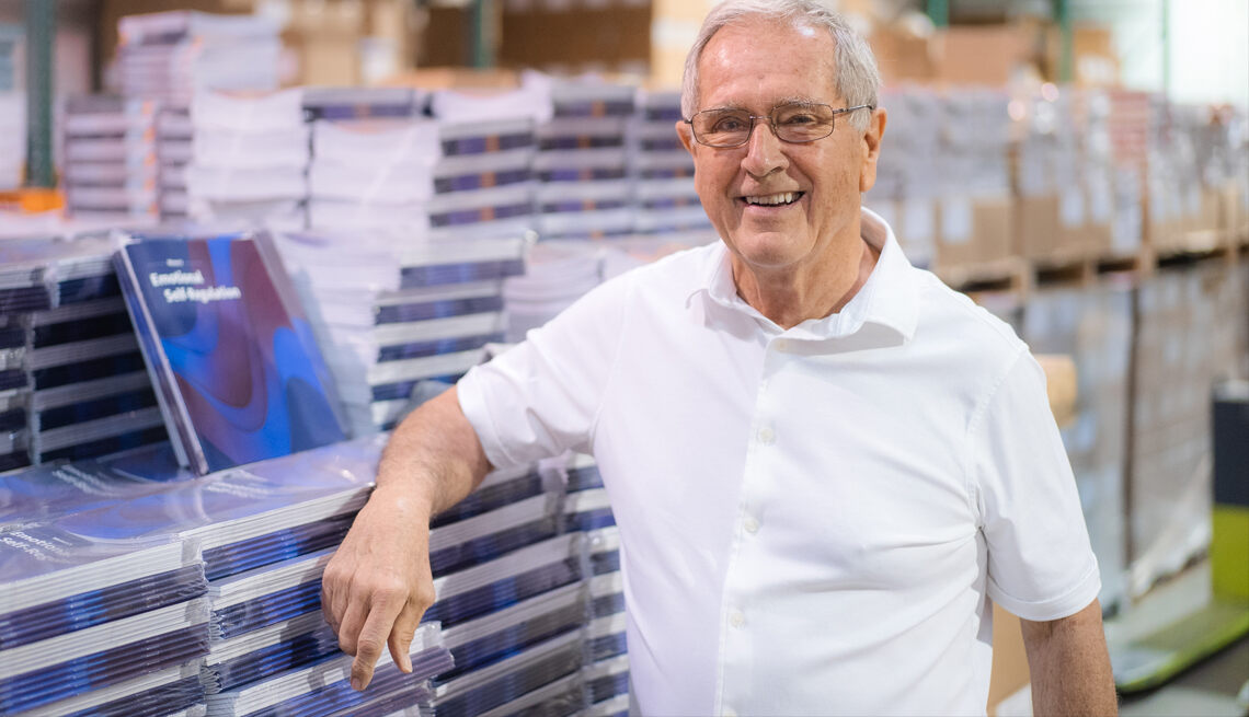 Author Don Kuhl standing in a warehouse next to stacks of his new book