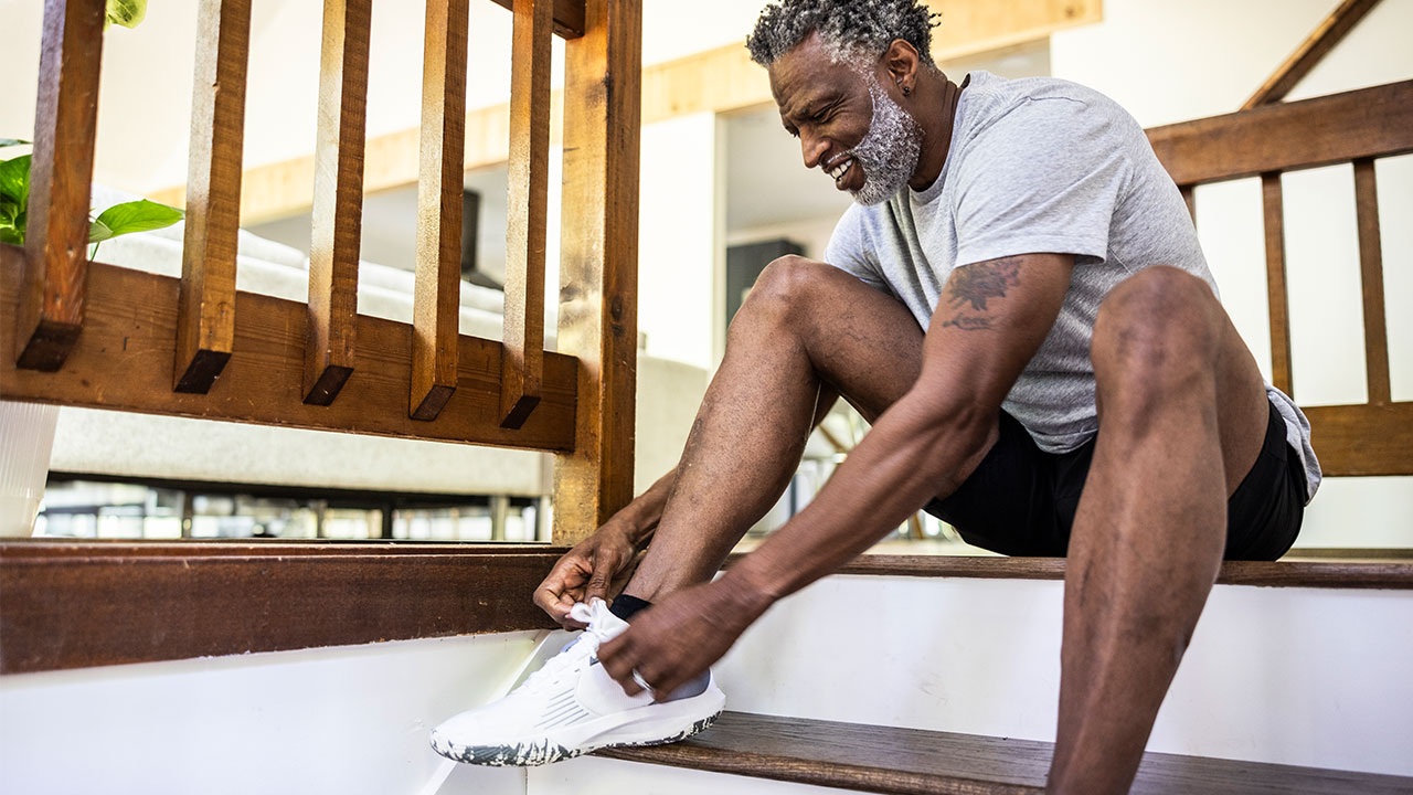 African-American man sits on porch to tie sneaker shoelace.