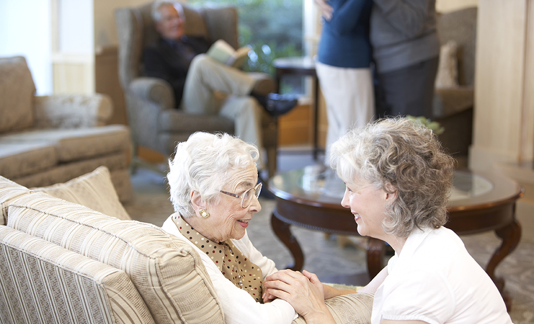A family gathering. An elderly woman speaking with a younger senior woman.
