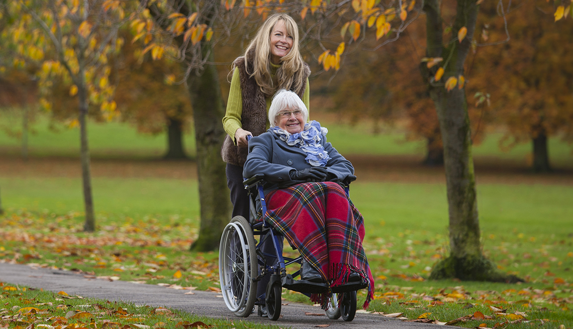 Caregiver pushing a woman in a wheelchair on a tree-lined path