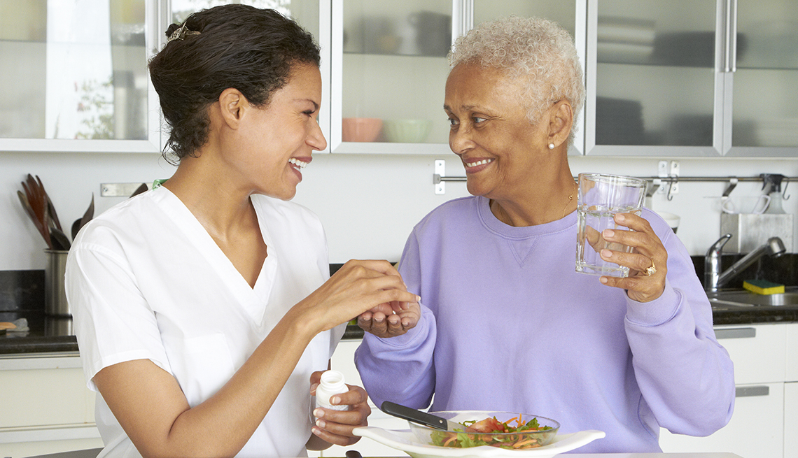 Home health aide giving her female care recipient her pills and a plate of lunch
