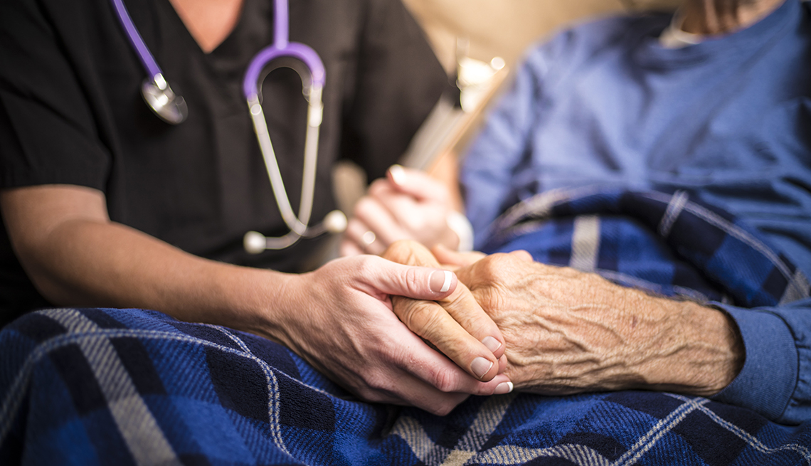Close up of a hospice nurse holding the hands of one of her patients