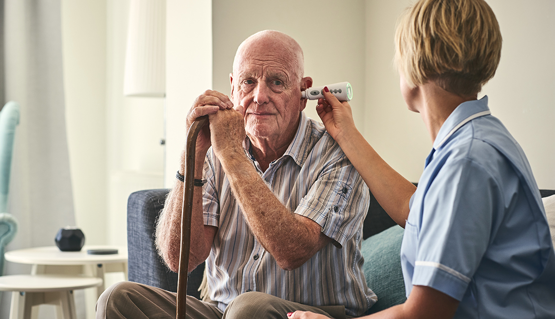 An in-home caregiving aide taking her patients temperature to screen him for the coronavirus