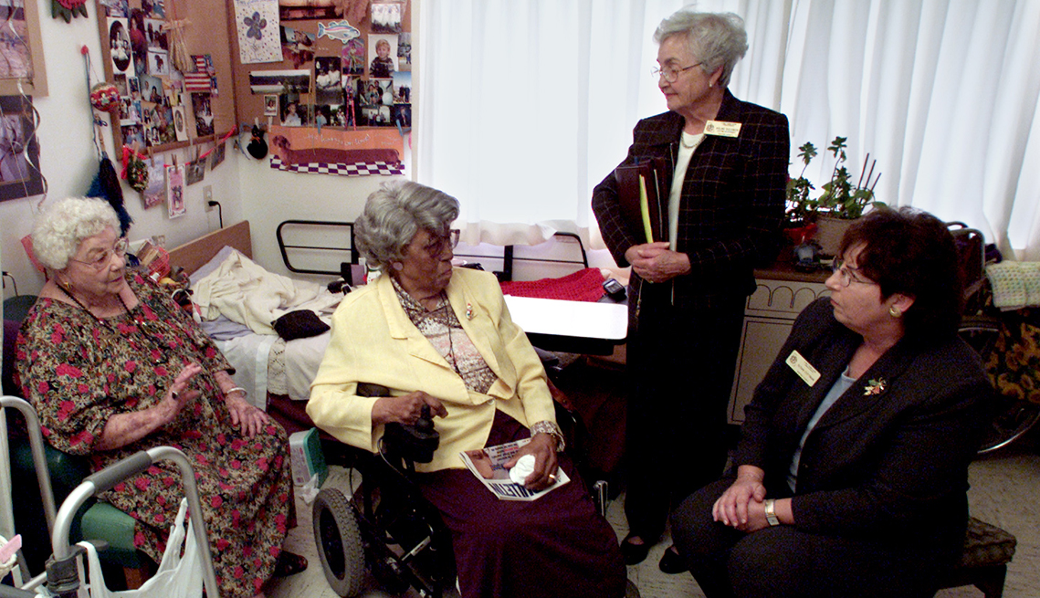 Two female nursing home residents in their room speak with two long term care ombudsman