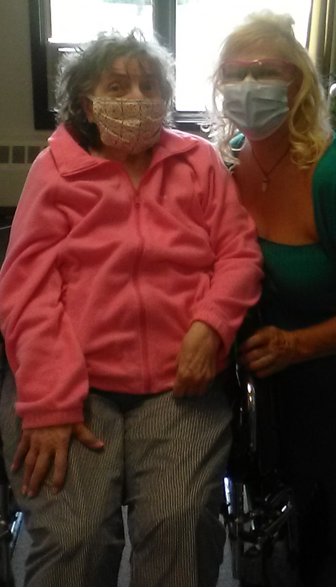 Woman and her mother who is seated in a wheelchair. Both are wearing face masks.