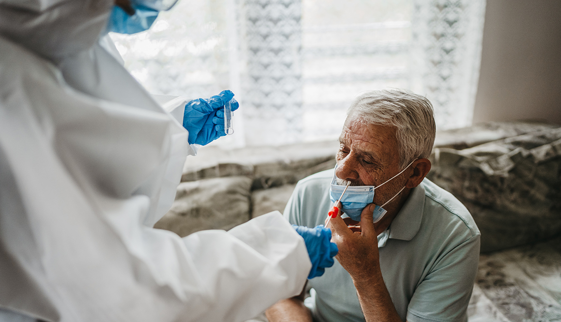 Un médico con traje de protección que toma la prueba de coronavirus con hisopo nasal de un residente de un hogar de ancianos masculino.