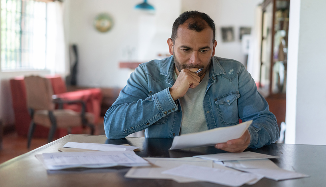 Un hombre de aspecto frustrado sentado en una mesa mirando a través de sus gastos y facturas.