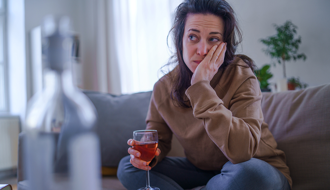 Una mujer que cuida a la familia sentada en su sofá con una copa de vino con aspecto estresado.