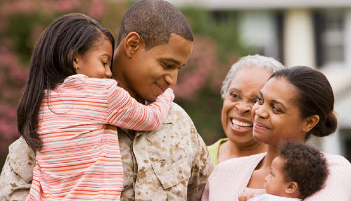 Man in a military uniform holding his daughter and smiling at his mother, wife and baby