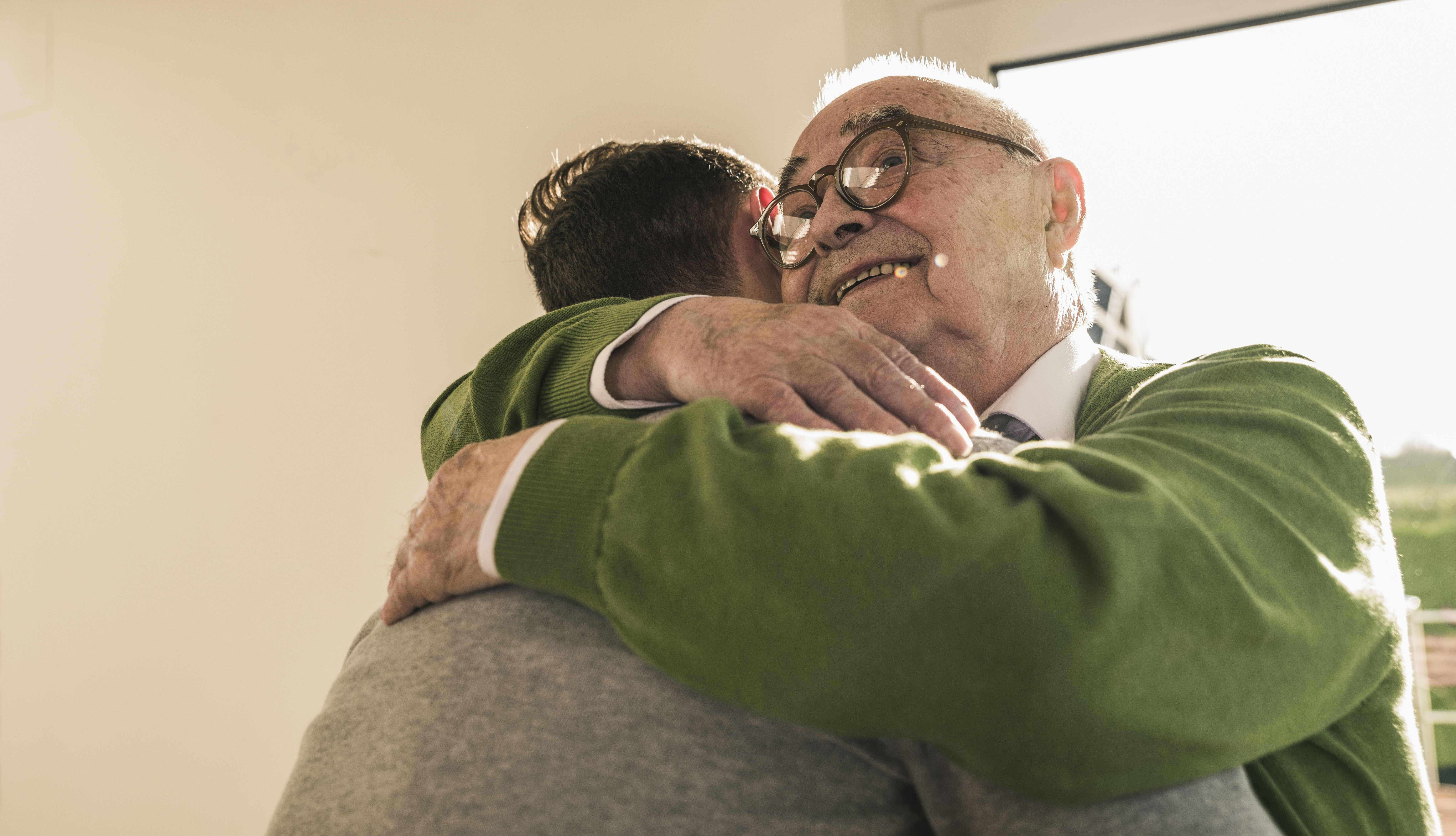 Un padre mayor abrazando a su hijo que lo visita en un hogar de ancianos.