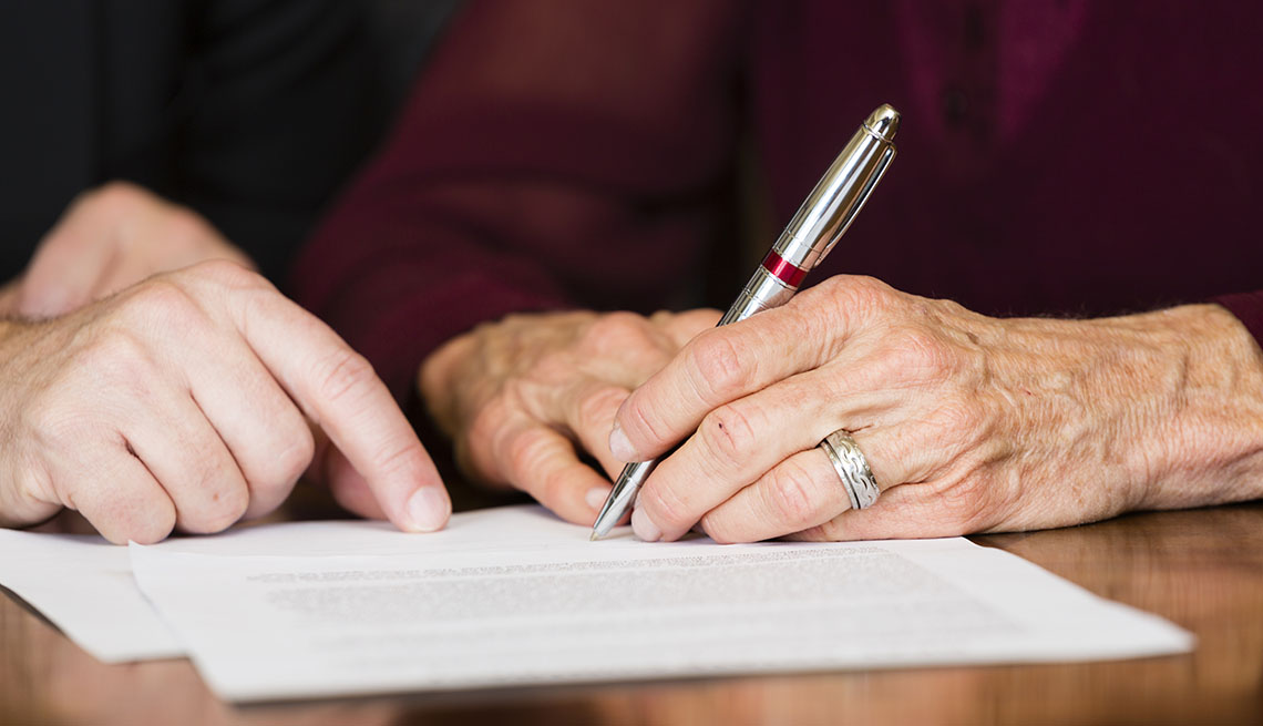 Una mujer mayor firma un documento.