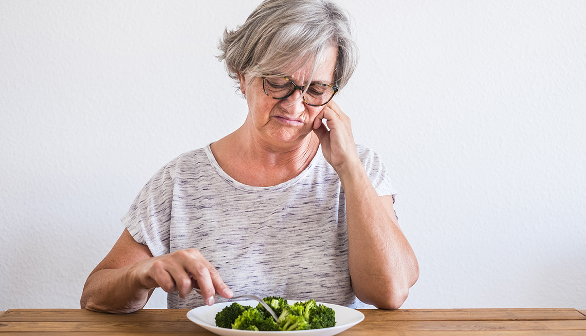 Una mujer mirando con cara de disgusto el brócoli en su plato de comida.