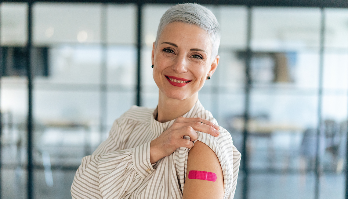 Portrait of woman showing her arm with band aid after coronavirus Covid-19 vaccine injection