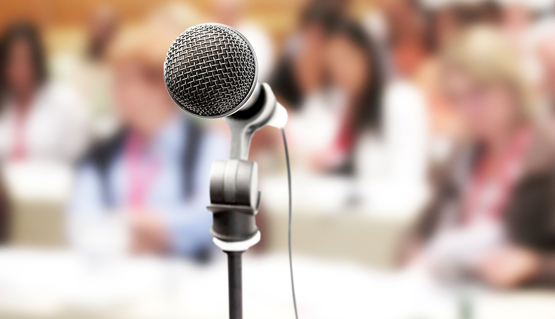 Close up on a vocal microphone in front of an out-of-focus audience at a meeting