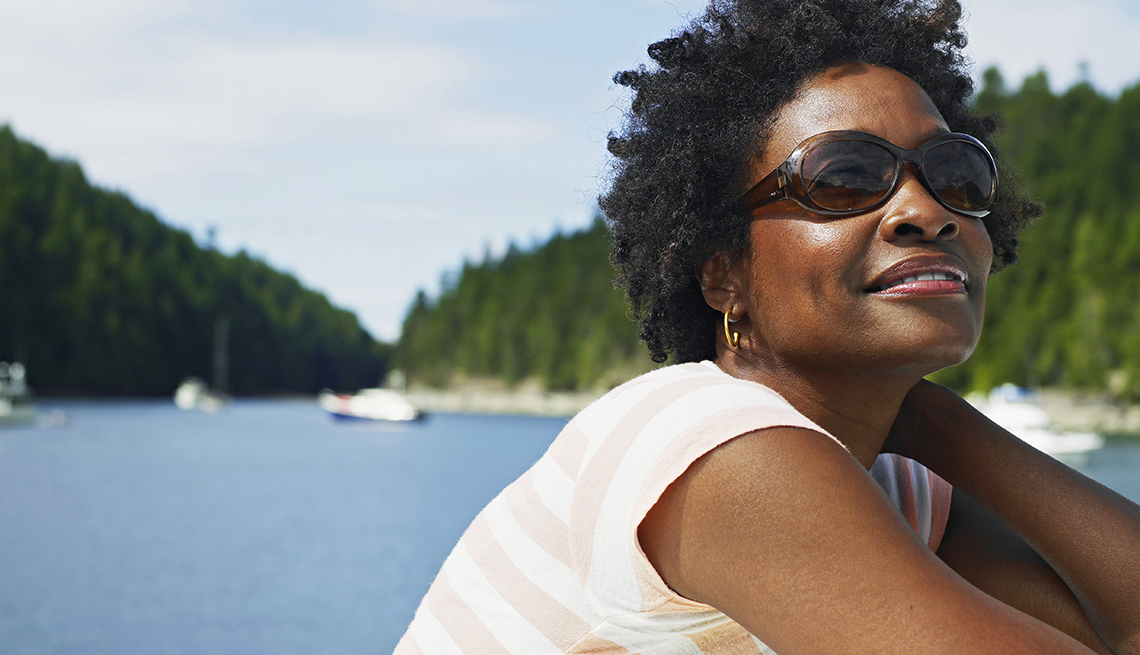 Close up of a woman wearing sunglasses to protect her eyes from the sun. A lake with boats is in the background