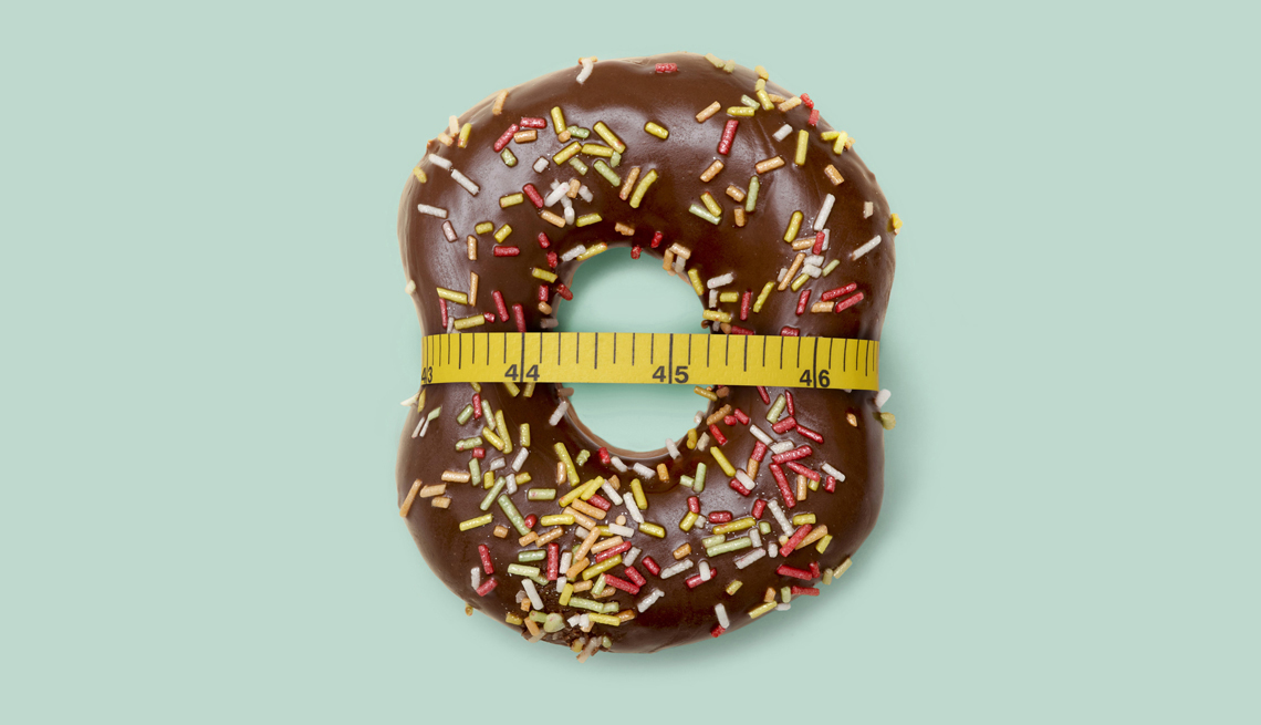 A chocolate donut with sprinkles with a tape measure wrapped around the center.
