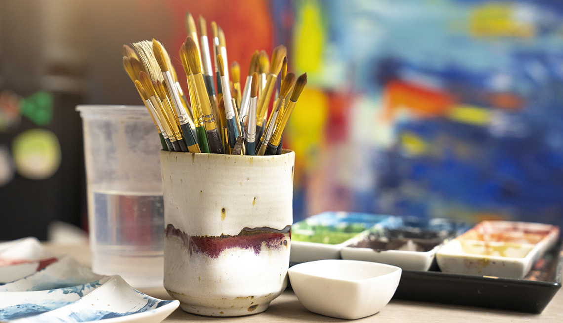artist's palette with oil paints and a cup full of paint brushes