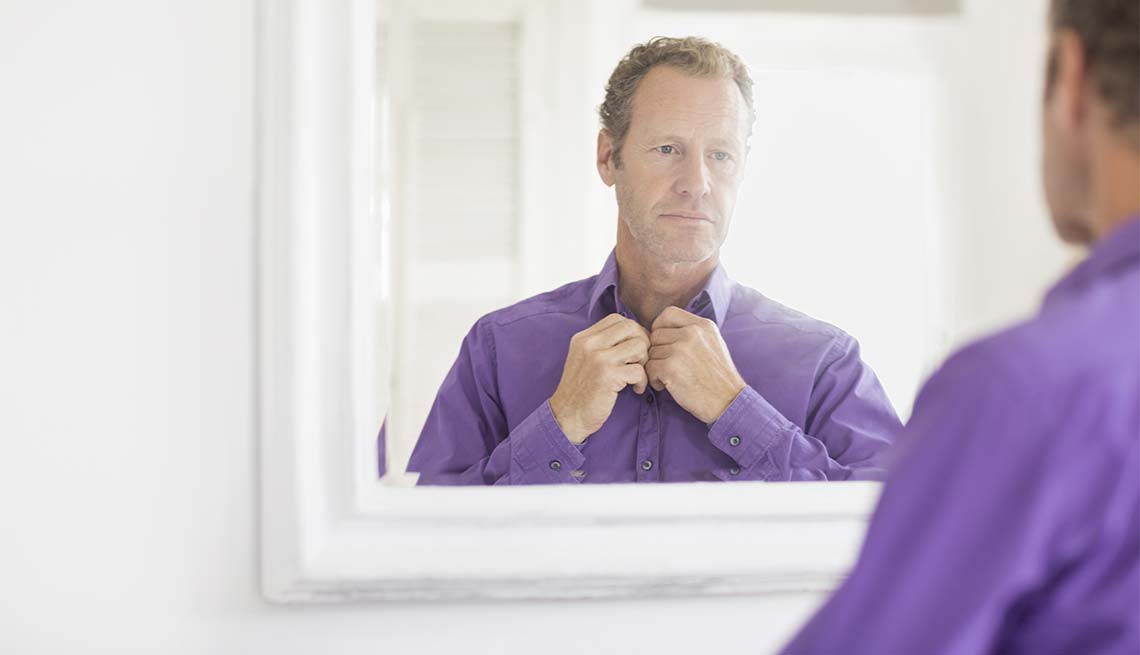 Hombre arreglándose la camisa en frente a un espejo en el baño - Cuidado del cabello para hombres de 50 años o más