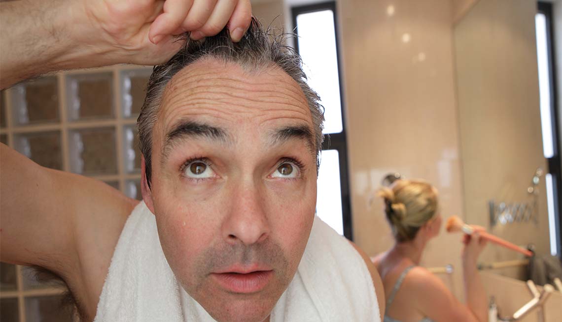 Hombre en el baño viendo su cabello en el espejo - Cuidado del cabello para hombres de 50 años o más
