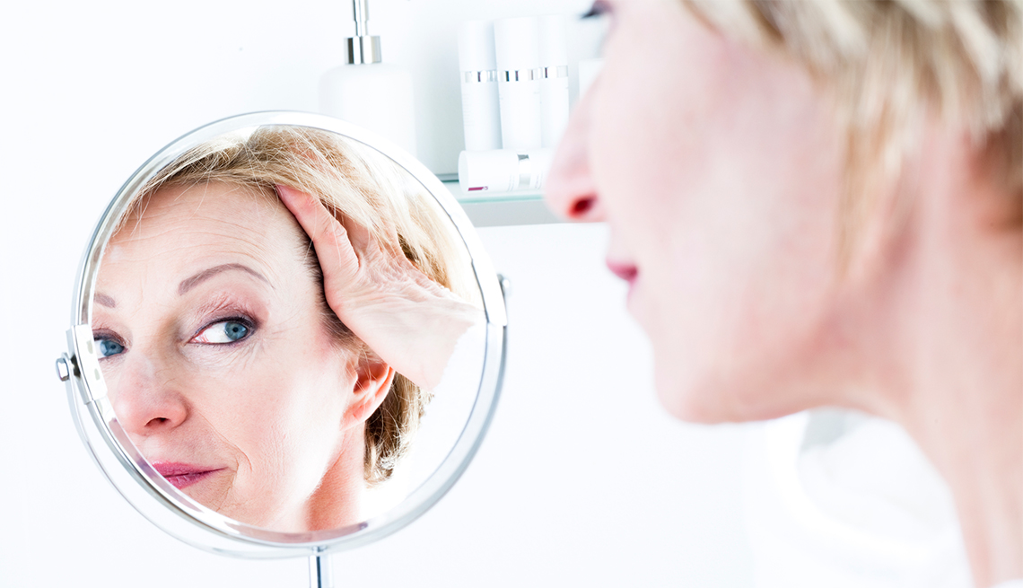 Mujer mirando su rostro en un espejo de aumento - Cremas para una piel sana y mantener un cutis joven