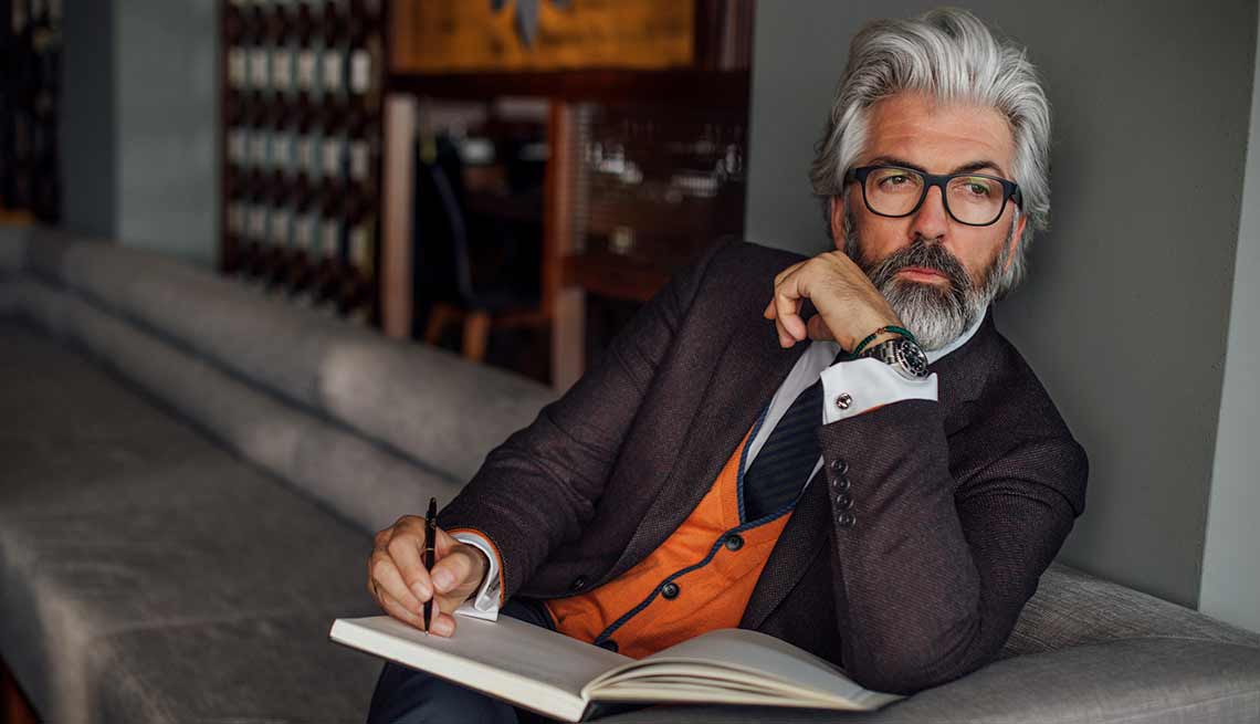 Hombre mayor en traje de corbata sentado en un sofá con un libro de apuntes y un lapicero - Secretos de moda de hombres sexy