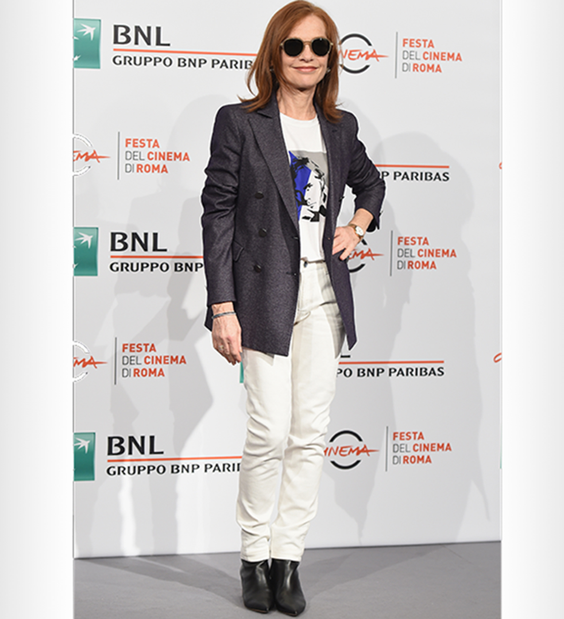 Isabelle Huppert in white jeans over black ankle booties with a blazer.