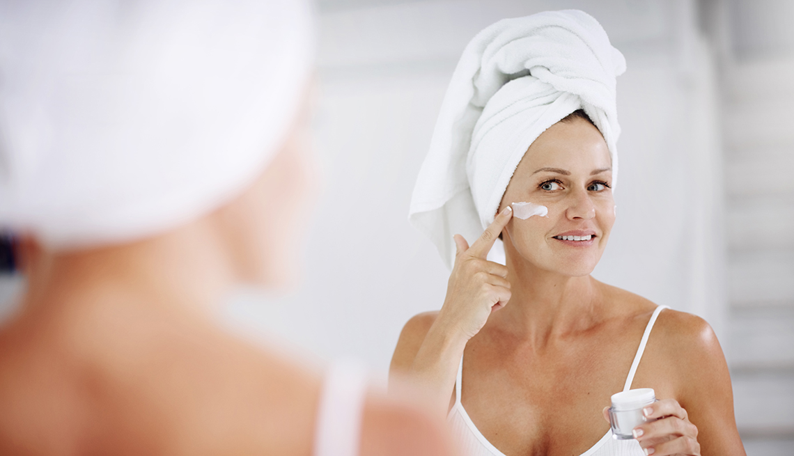 item 4 of Gallery image - A woman applying moisturizer to her face in front of a mirror